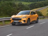 Ford Mustang Mach E GT geel aan het rijden op een berg weg schuinvoor