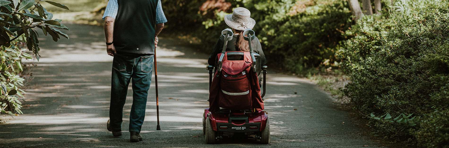 Man aan het wandelen met een stok en een vrouw in een scootmobiel